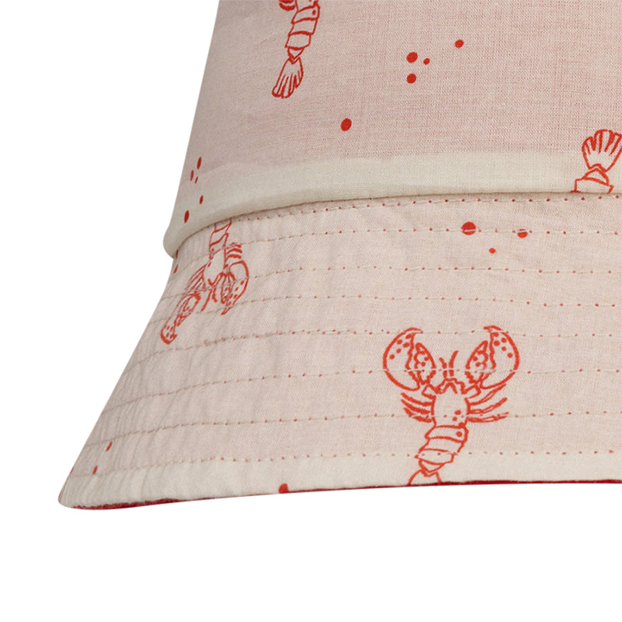 Close-up of a beige reversible hat with red lobster prints on a white background