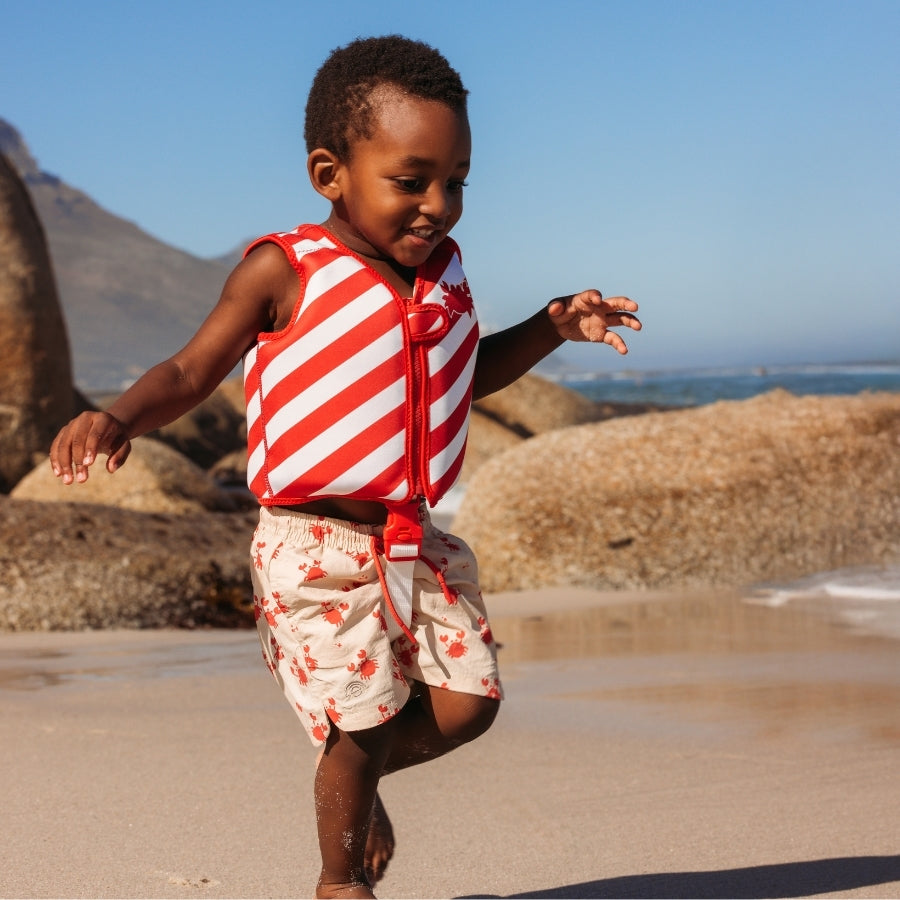 Child wearing a red and white striped life jacket on a beach with mountains in the background