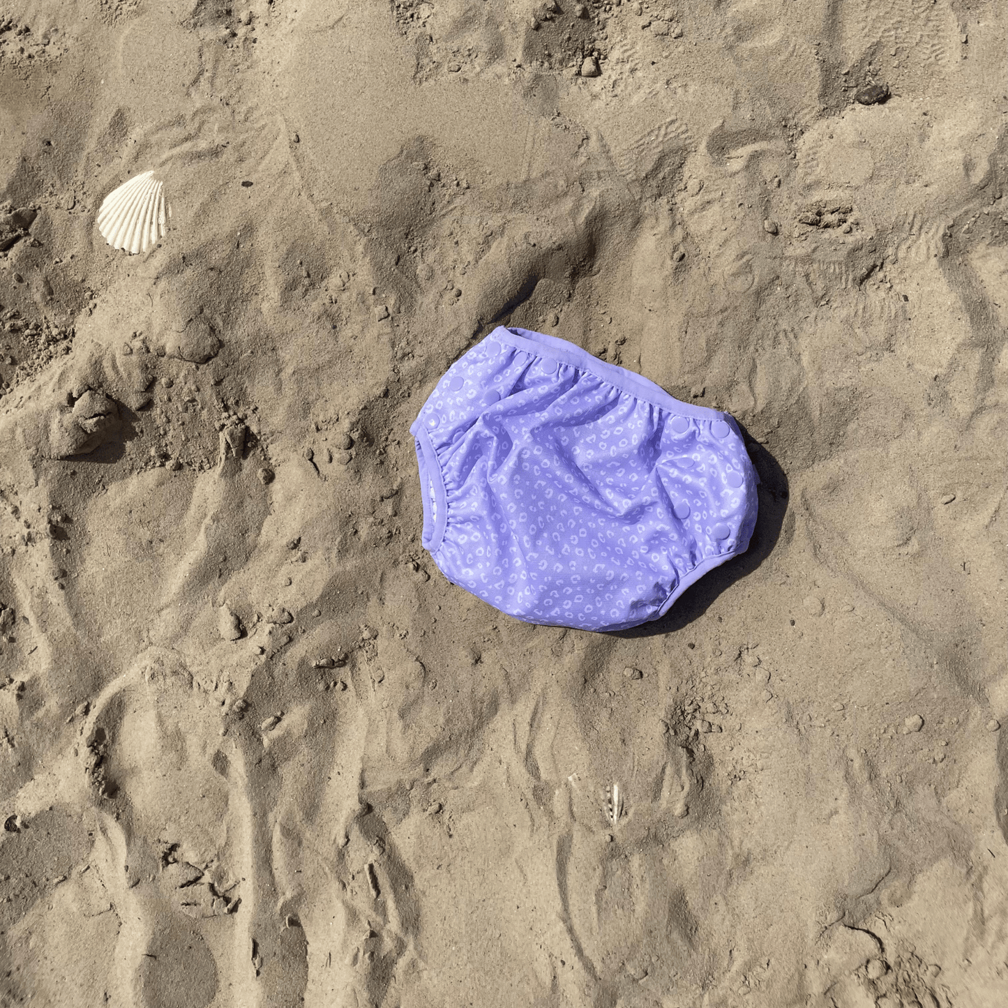 Purple swim diaper with white leopard pattern on sandy background