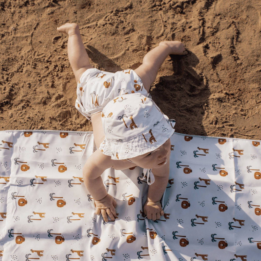 Baby lying on a jungle patterned towel on sand