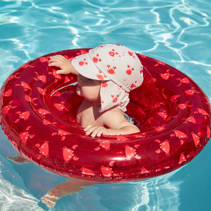 Child in a red crabby inflatable baby float with a crabby sun cap with a protective flap that shields the skin in clear blue water