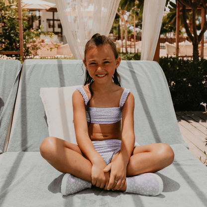 Young girl in a purple bikini sitting on a lounge chair outdoors.