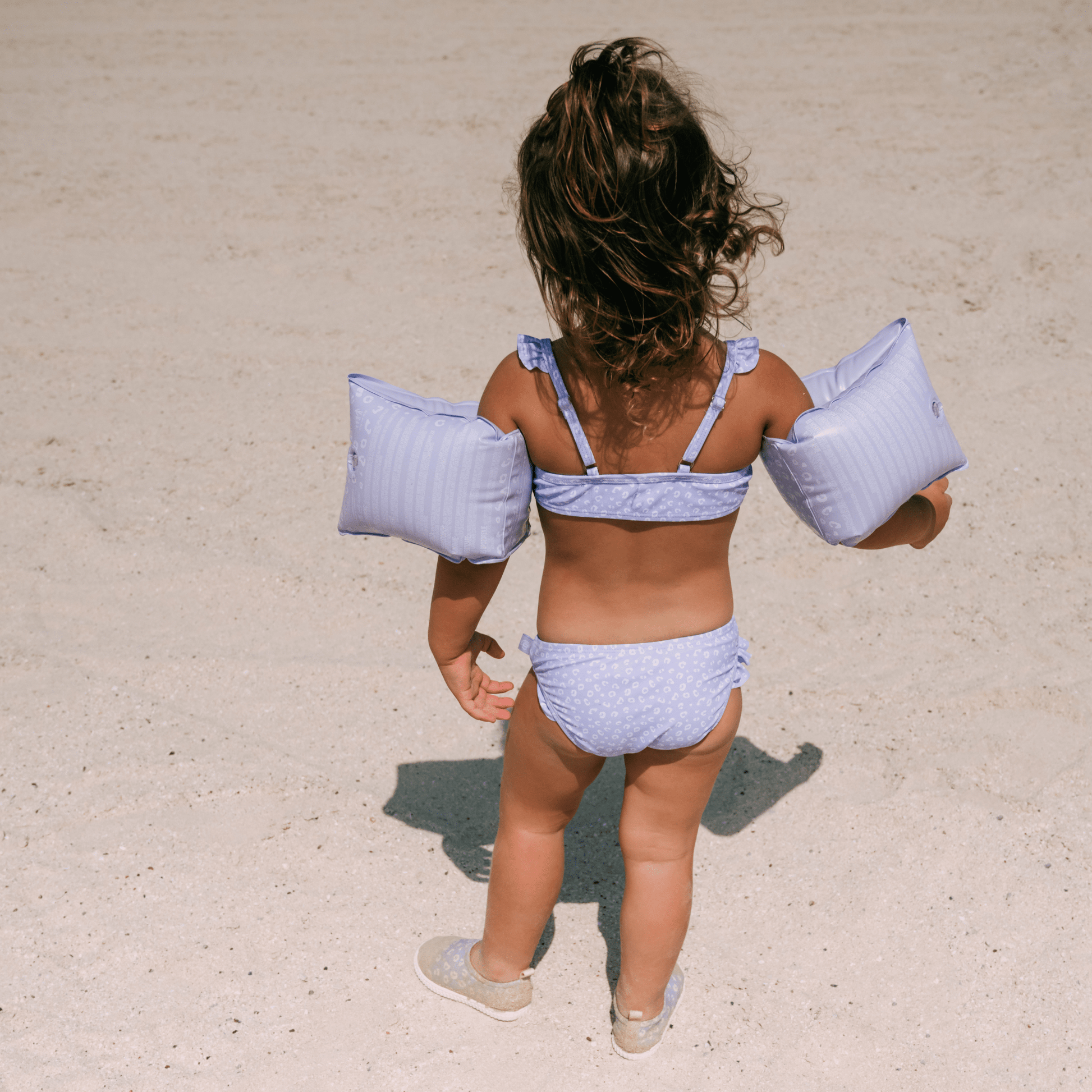 Child in a purple bikini with arm floats on a sandy beach