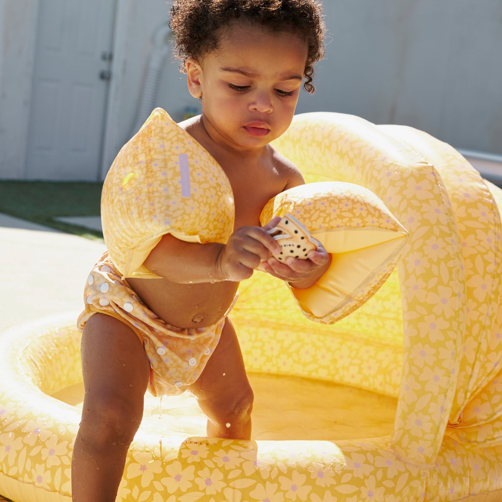 Child wearing a Florish Yellow diaper, florish yelloy arm bands playing in a yellow florish inflatable pool outdoors