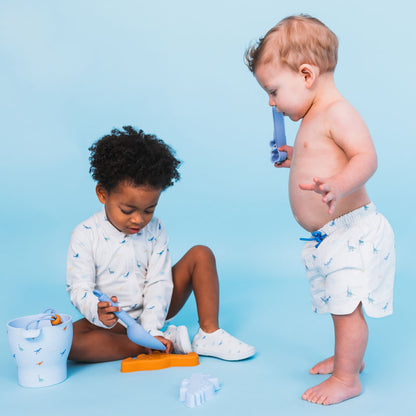 Two children playing with toys wearing the dino swimshirt and swim short on a blue background