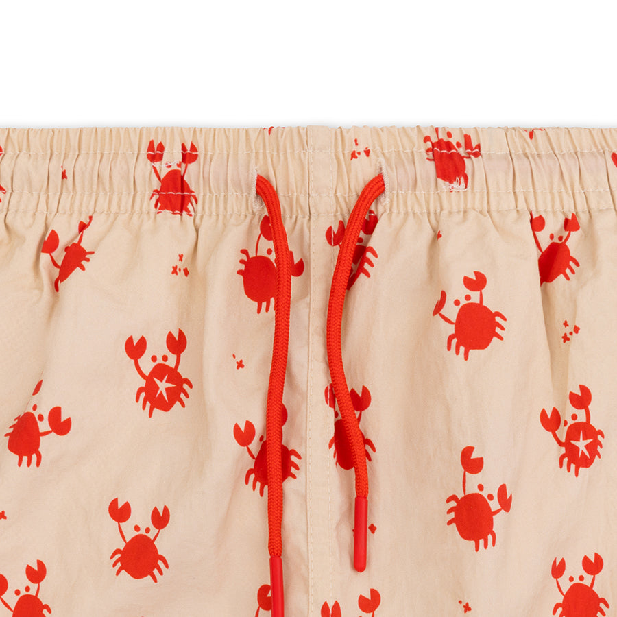 Close-up of beige swim shorts with red crab pattern on a white background