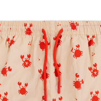 Close-up of beige swim shorts with red crab pattern on a white background