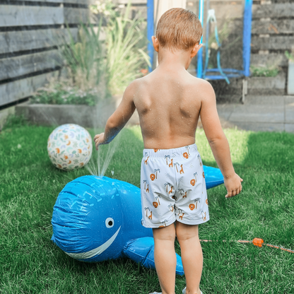Child playing with a blue whale-shaped sprinkler in a garden