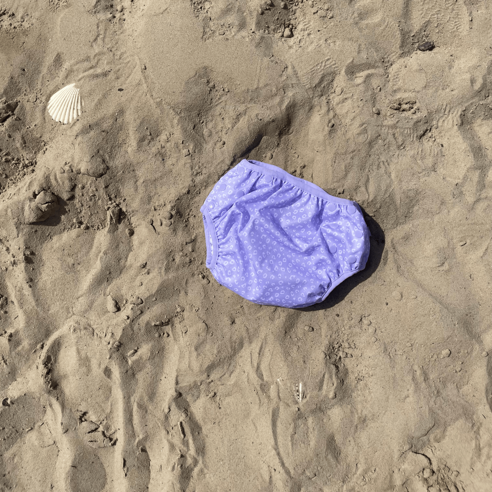 Purple swim diaper with white leopard pattern on sandy background