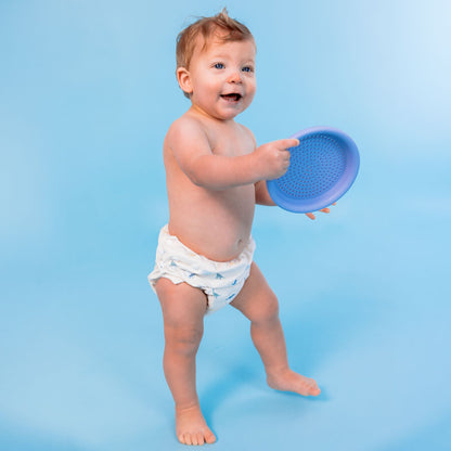 Baby holding a blue plastic toy against a light blue background wearing a swim diaper with dinosaur pattern