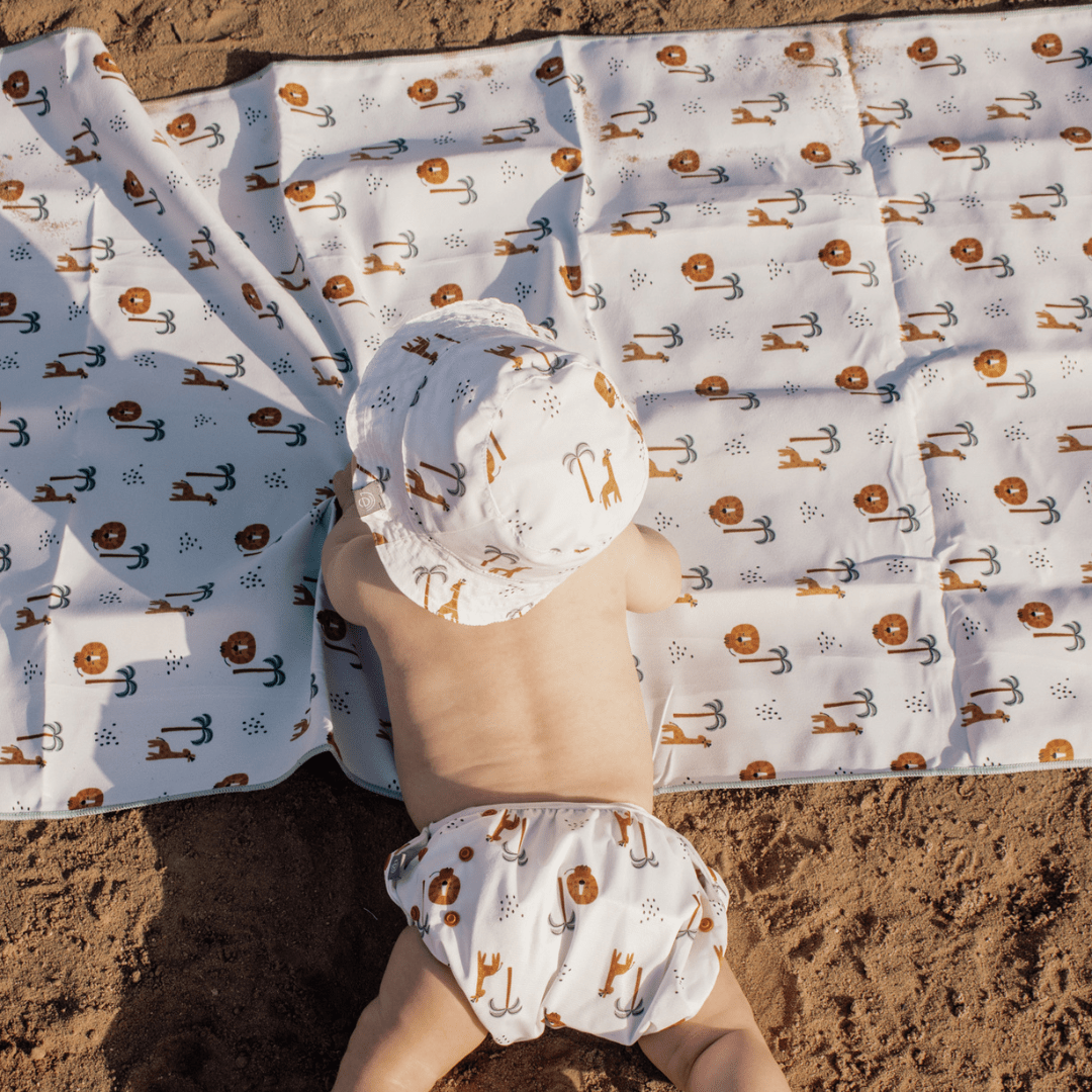 Child wearing a jungle-themed outfit and hat on a patterned towel on the beach