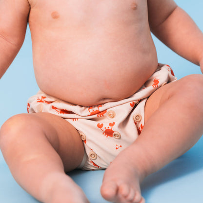 Baby wearing a swim diaper with a crab pattern on a blue background