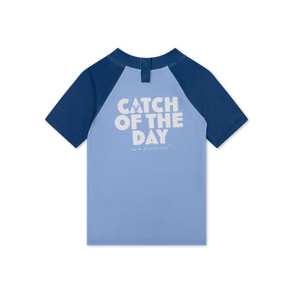 Blue and navy swimming shirt with 'Catch of the Day' text on a white background