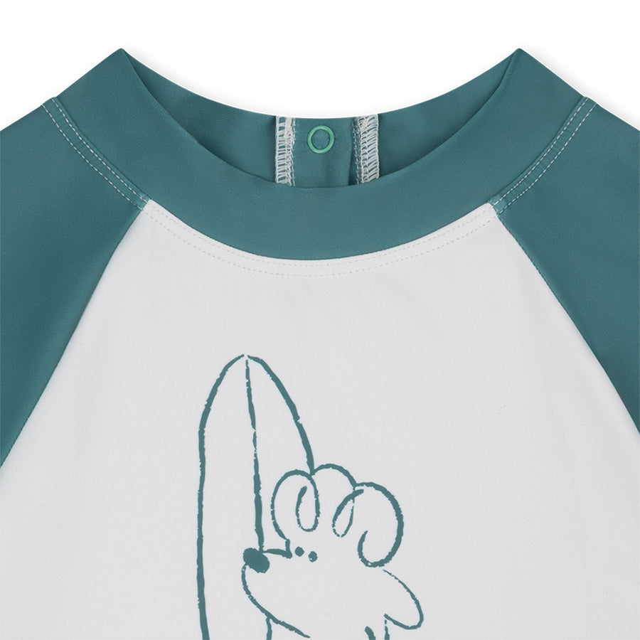 Close-up of a children's shirt with green sleeves and collar, featuring a cartoon dog on a white background.