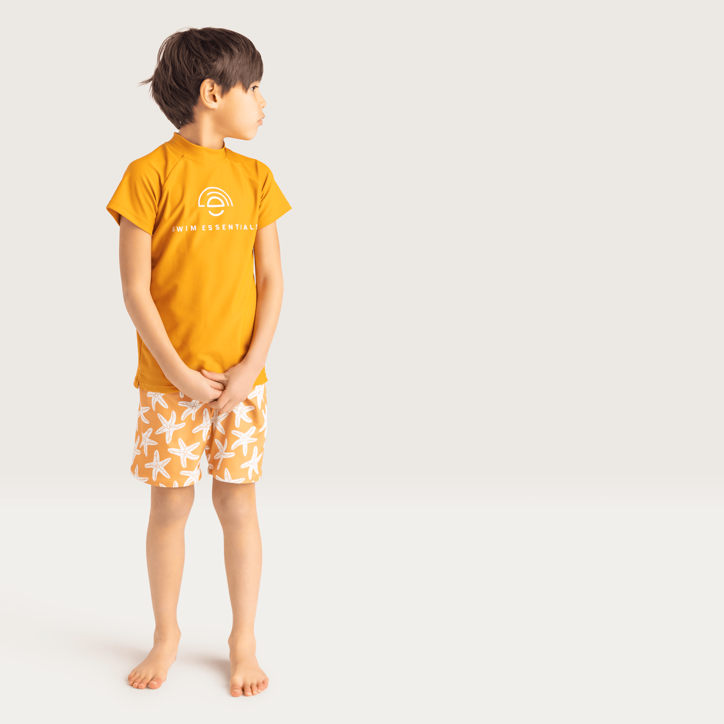 A child wearing a orange t-shirt with orange swim shorts with a white seastar print