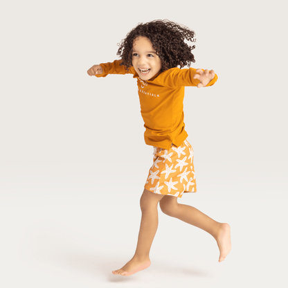 A child wearing a orange t-shirt with orange swim shorts with a white seastar print