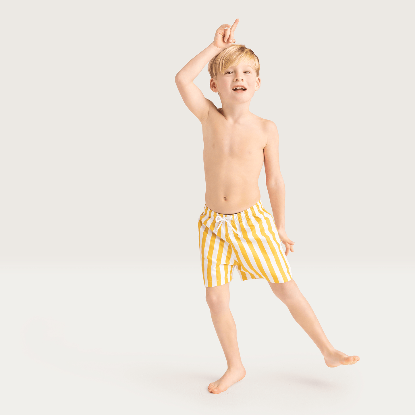 Young boy wearing yellow striped swim shorts on a white background