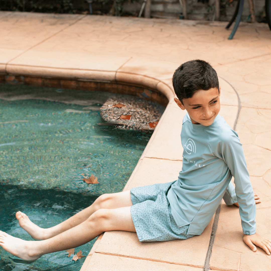Child sitting by a pool wearing a light blue swimming t-shirt.