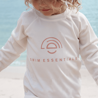 Child wearing a white long-sleeve shirt with 'Swim Essentials' logo against a light blue background