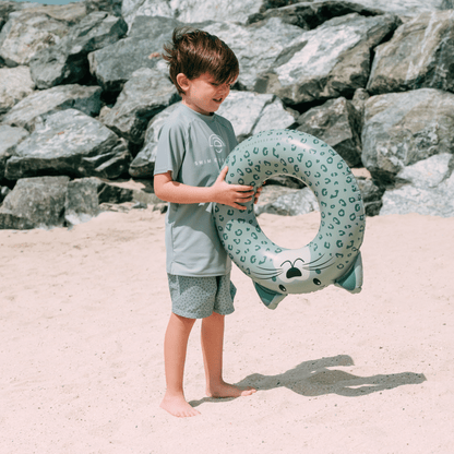 Child holding a shark-shaped inflatable ring on a beach with rocks in the background