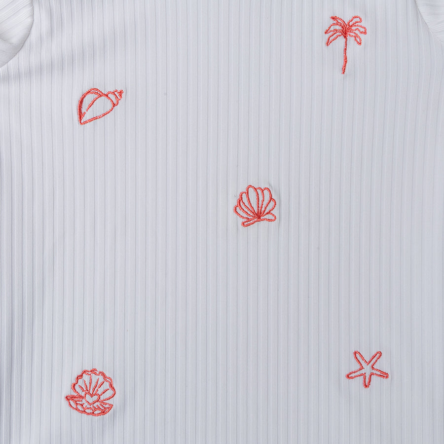White shirt with red embroidered patterns of a palm tree, shell, and leaf on a textured background.
