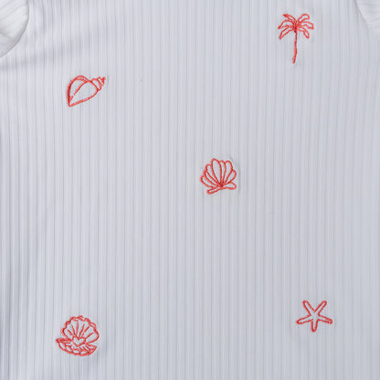 White shirt with red embroidered patterns of a palm tree, shell, and leaf on a textured background.