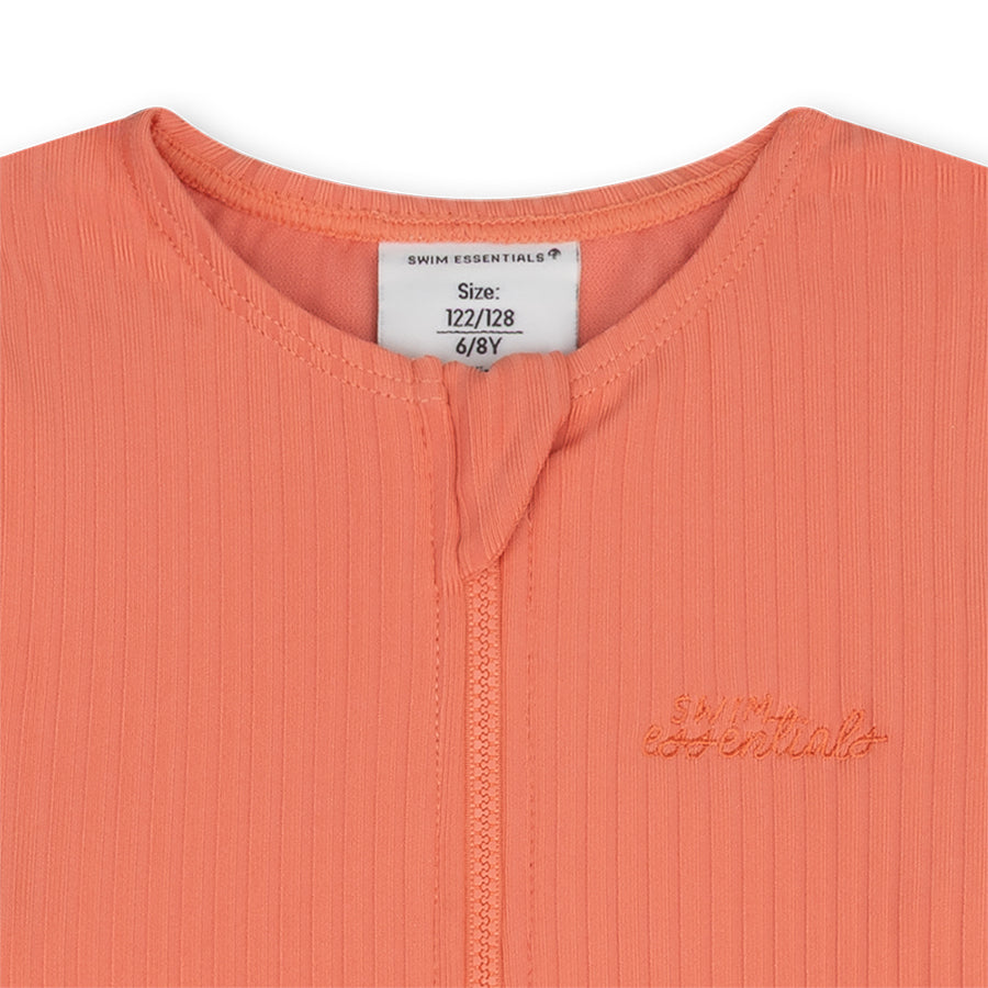 Close-up of a coral-colored garment with a brand logo and size label on a white background